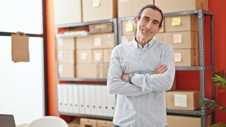Téléchargez les photos : Homme d'âge moyen commerce électronique travailleur d'affaires debout avec les bras croisés geste souriant au bureau - en image libre de droit