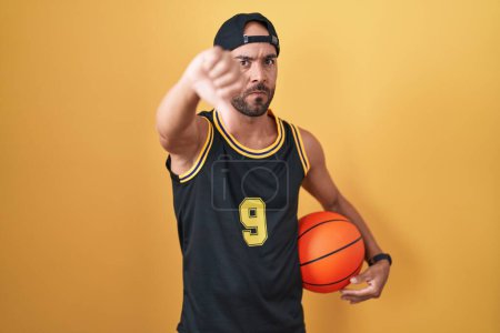 Photo for Middle age bald man holding basketball ball over yellow background looking unhappy and angry showing rejection and negative with thumbs down gesture. bad expression. - Royalty Free Image
