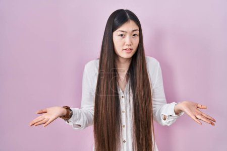 Téléchargez les photos : Chinoise jeune femme debout sur fond rose sans aucune idée et confondue avec les bras ouverts, aucune idée concept. - en image libre de droit