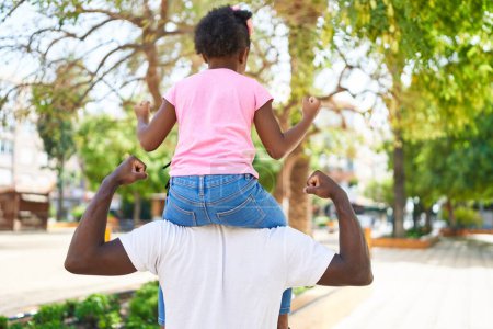 Foto de Father and daughter holding girl on shoulders standing on back view at park - Imagen libre de derechos