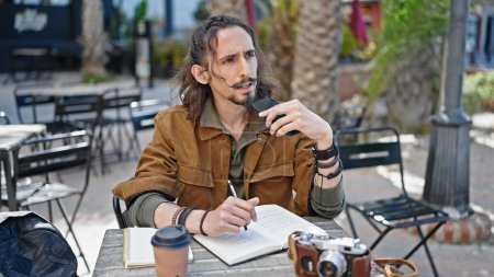 Téléchargez les photos : Jeune homme hispanique touriste envoyer un message vocal par smartphone assis sur la table à la terrasse du café - en image libre de droit