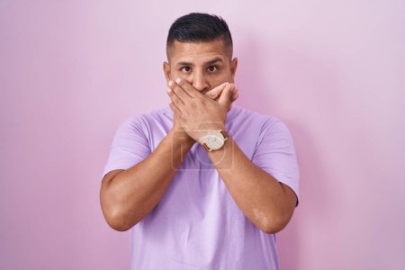 Photo for Young hispanic man standing over pink background shocked covering mouth with hands for mistake. secret concept. - Royalty Free Image