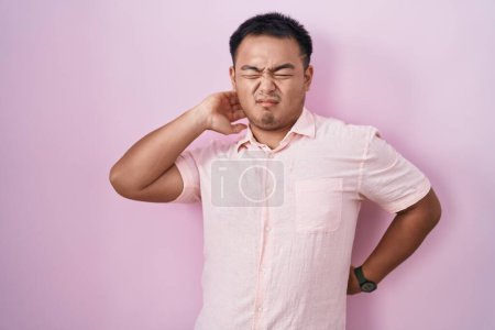 Photo for Chinese young man standing over pink background suffering of neck ache injury, touching neck with hand, muscular pain - Royalty Free Image