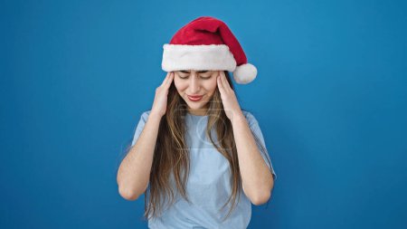 Photo for Young beautiful hispanic woman wearing christmas hat having headache over isolated blue background - Royalty Free Image