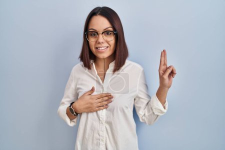 Photo for Young hispanic woman standing over white background smiling swearing with hand on chest and fingers up, making a loyalty promise oath - Royalty Free Image