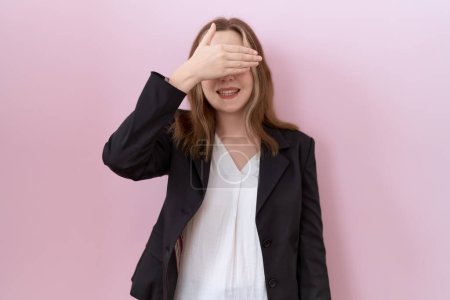 Téléchargez les photos : Jeune femme d'affaires caucasienne portant une veste noire souriant et riant avec la main sur le visage couvrant les yeux pour la surprise. concept aveugle. - en image libre de droit