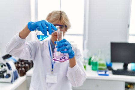 Téléchargez les photos : Jeune homme blond scientifique versant du liquide sur éprouvette au laboratoire - en image libre de droit