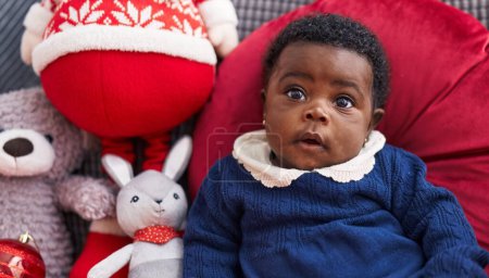 Téléchargez les photos : Bébé afro-américain assis sur un canapé avec décor de Noël à la maison - en image libre de droit