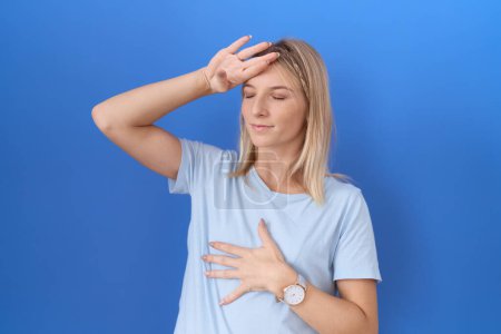 Foto de Mujer caucásica joven que usa una camiseta azul casual tocando la frente por enfermedad y fiebre, gripe y resfriado, virus enfermo - Imagen libre de derechos