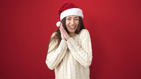 Téléchargez les photos : Jeune belle femme hispanique souriant confiant portant un chapeau de Noël sur fond rouge isolé - en image libre de droit
