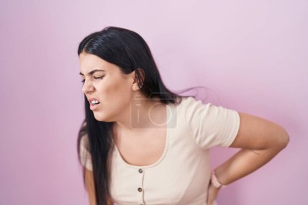 Photo for Young hispanic woman standing over pink background suffering of backache, touching back with hand, muscular pain - Royalty Free Image