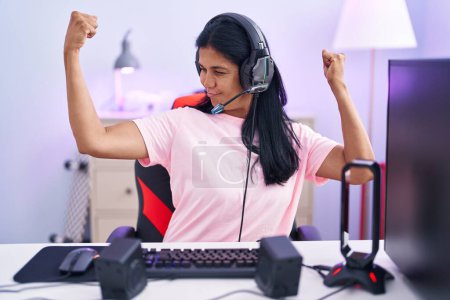 Photo for Mature hispanic woman playing video games at home showing arms muscles smiling proud. fitness concept. - Royalty Free Image
