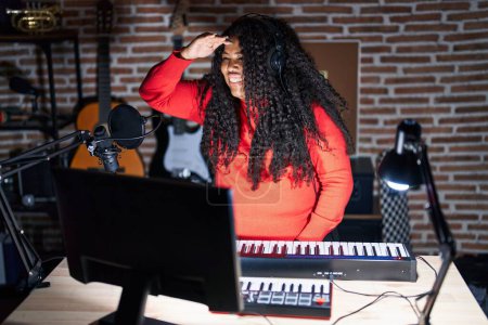 Téléchargez les photos : Plus taille hispanique femme jouant du piano au studio de musique très heureux et souriant regardant loin avec la main au-dessus de la tête. concept de recherche. - en image libre de droit