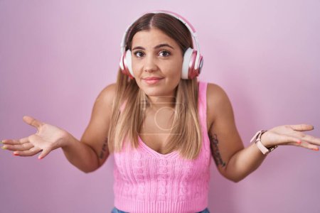 Photo for Young blonde woman listening to music using headphones clueless and confused with open arms, no idea concept. - Royalty Free Image