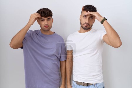 Téléchargez les photos : Couple homosexuel gay debout sur fond blanc inquiet et stressé par un problème avec la main sur le front, nerveux et anxieux pour la crise - en image libre de droit