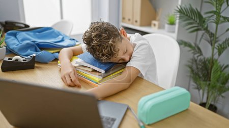 Photo for Adorable blond boy student, tired yet diligent, caught sleeping on his study books in a cosy classroom setting - Royalty Free Image