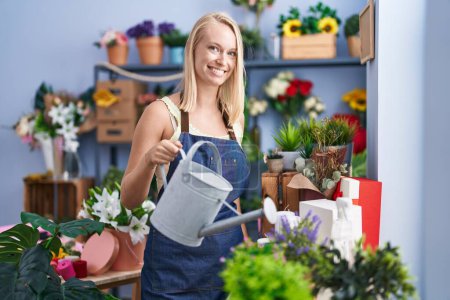 Photo for Young blonde woman florist smiling confident watering plant at florist store - Royalty Free Image