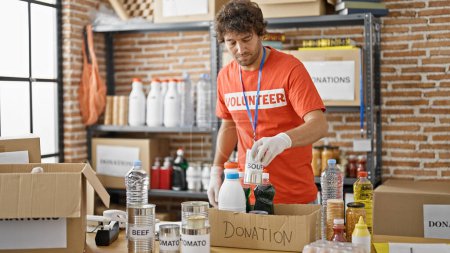 Téléchargez les photos : Jeune homme hispanique volontaire emballage boîte de carton alimentaire pour faire un don au centre de charité - en image libre de droit