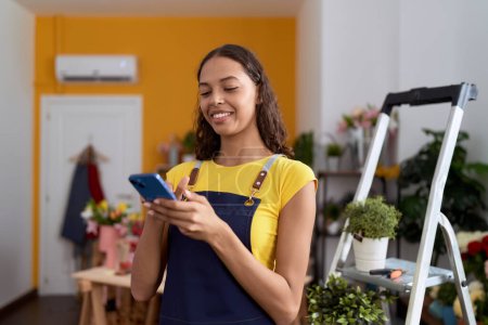 Photo for Young african american woman florist smiling confident using smartphone at flower shop - Royalty Free Image
