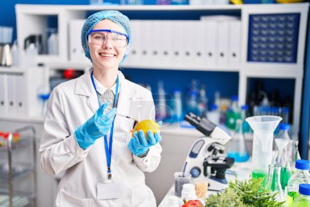 Foto de Mujer joven rubia científica inyectando limón en el laboratorio - Imagen libre de derechos