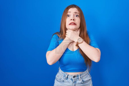 Photo for Redhead woman standing over blue background shouting suffocate because painful strangle. health problem. asphyxiate and suicide concept. - Royalty Free Image