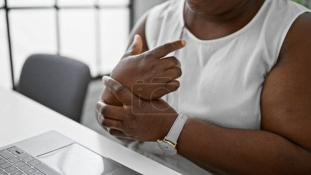 Photo for Overworked african american businesswoman grips her aching wrist, struggling with pain while working on laptop indoors at the office - Royalty Free Image