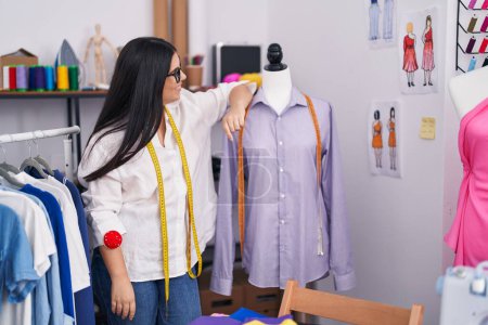 Photo for Young beautiful hispanic woman tailor smiling confident leaning on manikin at atelier - Royalty Free Image