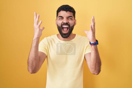 Photo for Hispanic man with beard standing over yellow background celebrating mad and crazy for success with arms raised and closed eyes screaming excited. winner concept - Royalty Free Image