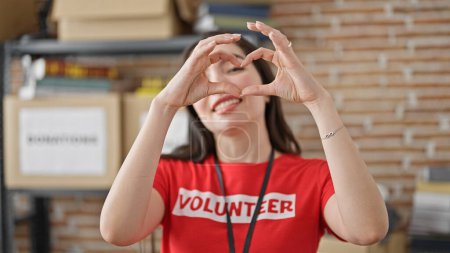 Photo for Young beautiful hispanic woman volunteer doing heart gesture smiling at charity center - Royalty Free Image