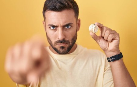 Photo for Handsome hispanic man holding tether cryptocurrency coin pointing with finger to the camera and to you, confident gesture looking serious - Royalty Free Image