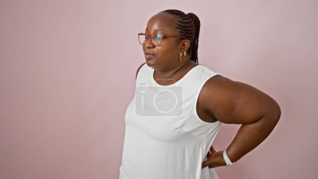 Photo for Worried african american woman, plus size with braids, standing alone, suffering serious backache over isolated pink background. worry of spinal injury showing on her hurting face. - Royalty Free Image