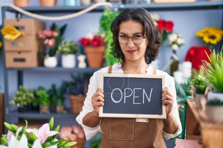Photo for Young hispanic woman working at florist holding open sign clueless and confused expression. doubt concept. - Royalty Free Image