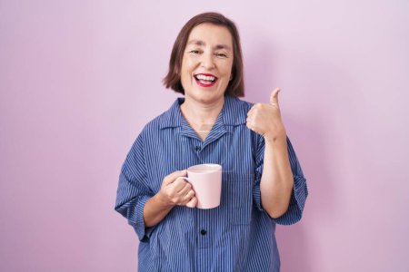 Foto de Mujer hispana de mediana edad bebiendo una taza de café haciendo un gesto feliz con la mano. aprobando la expresión mirando a la cámara mostrando éxito. - Imagen libre de derechos