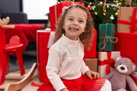 Photo for Adorable blonde girl smiling confident sitting on floor by christmas tree at home - Royalty Free Image