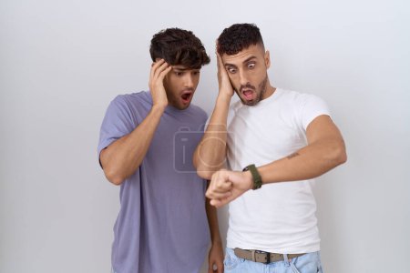 Foto de Homosexual pareja gay de pie sobre blanco fondo mirando el reloj tiempo preocupado, miedo de llegar tarde - Imagen libre de derechos