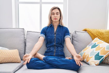 Photo for Young woman doing yoga exercise sitting on sofa at home - Royalty Free Image