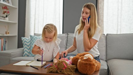 Photo for Relaxed mother-daughter bond, caucasian mum and little girl draw on notebook, engaging in serious talk over smartphone at home - Royalty Free Image