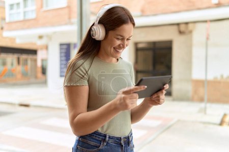 Téléchargez les photos : Jeune belle femme souriante confiante regarder la vidéo sur touchpad à la rue - en image libre de droit