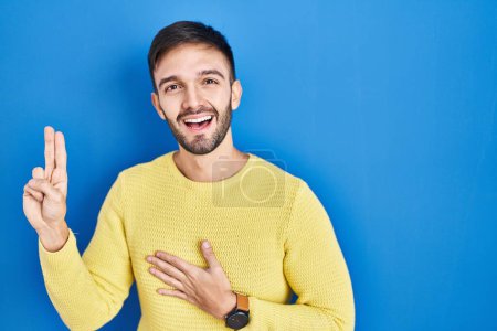 Photo for Hispanic man standing over blue background smiling swearing with hand on chest and fingers up, making a loyalty promise oath - Royalty Free Image