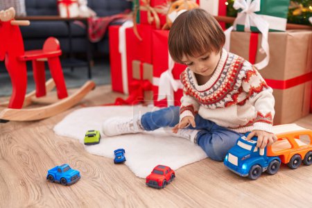 Photo for Adorable toddler playing with truck toy sitting on floor by christmas tree at home - Royalty Free Image