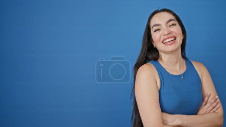 Photo for Young beautiful hispanic woman standing with arms crossed gesture saying yes with hand over isolated blue background - Royalty Free Image