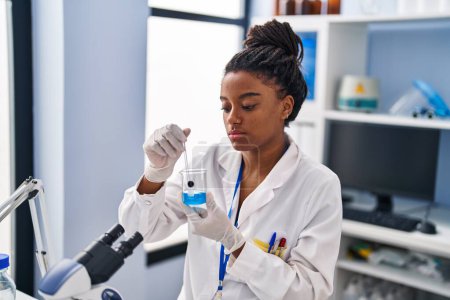 Téléchargez les photos : Femme scientifique afro-américaine mélangeant du liquide sur verre au laboratoire - en image libre de droit