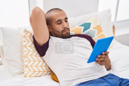 Téléchargez les photos : Young latin man using touchpad lying on bed at bedroom - en image libre de droit