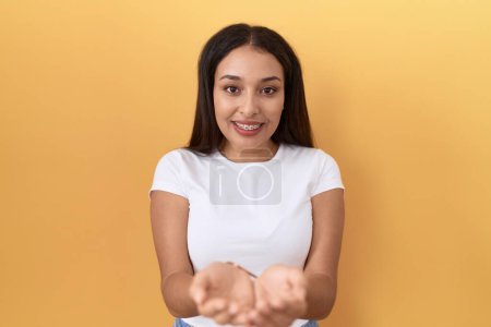 Photo for Young arab woman wearing casual white t shirt over yellow background smiling with hands palms together receiving or giving gesture. hold and protection - Royalty Free Image
