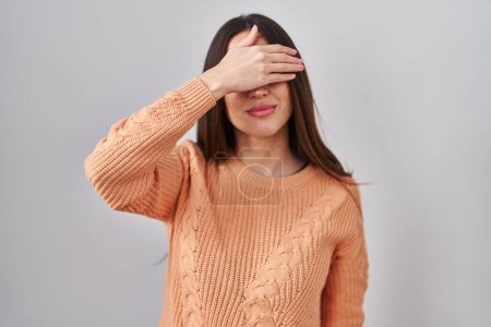 Téléchargez les photos : Jeune femme brune debout sur fond blanc couvrant les yeux avec la main, l'air grave et triste. concept de non-visibilité, de dissimulation et de rejet - en image libre de droit