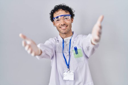 Téléchargez les photos : Un homme hispanique travaillant au laboratoire scientifique regardant la caméra souriant à bras ouverts pour un câlin. expression joyeuse embrassant le bonheur. - en image libre de droit