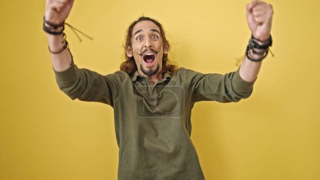 Téléchargez les photos : Jeune homme hispanique souriant confiant debout avec geste gagnant sur fond jaune isolé - en image libre de droit