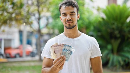 Téléchargez les photos : Jeune homme hispanique tenant des pesos mexicains au parc - en image libre de droit