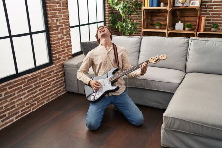 Téléchargez les photos : Jeune homme caucasien jouant de la guitare électrique sur le sol à la maison - en image libre de droit