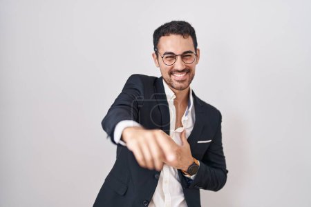 Foto de Hombre hispano de negocios guapo parado sobre fondo blanco riéndose de ti, señalando con el dedo a la cámara con la mano sobre el cuerpo, expresión de vergüenza - Imagen libre de derechos